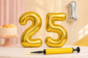 Air-filled gold foil number 25 balloons on a table with a balloon pump